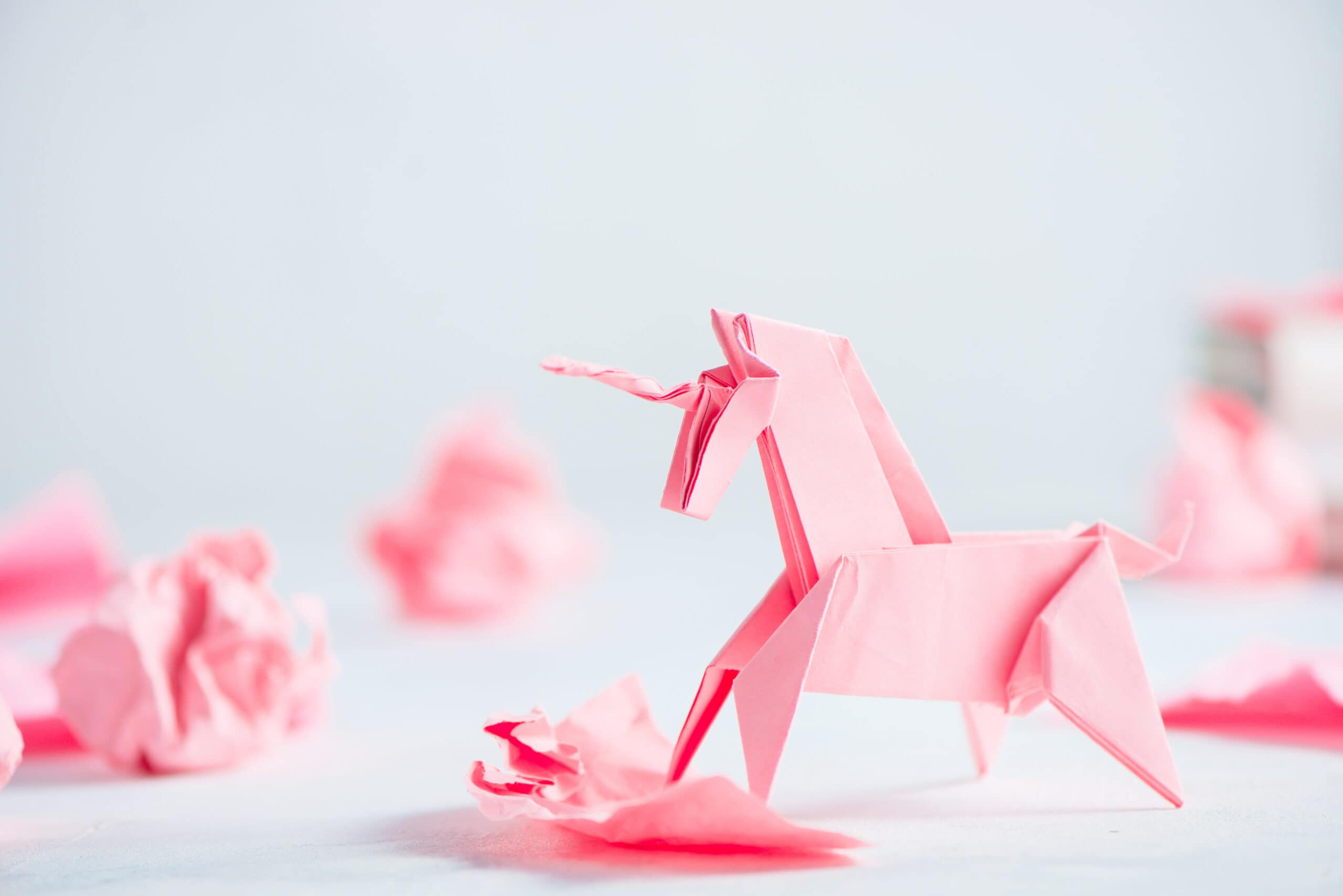 Pink origami unicorn with crumpled paper balls. Creative process is writing, light background