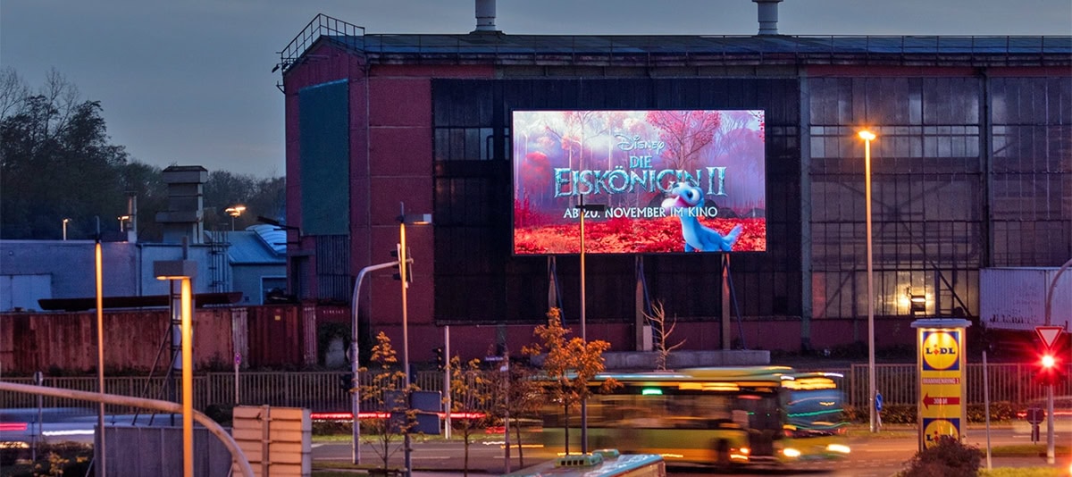 Leuchtreklame für einen Disney-Film bei Abenddämmerung auf einer Industriegebäude; vorbeifahrender Bus.