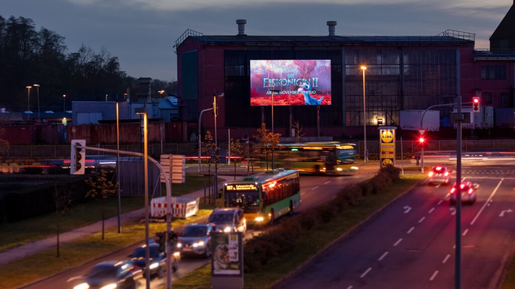 Verkehr bei Abenddämmerung, beleuchtete Werbetafel, Bus in Bewegung, Autolichter leuchten.