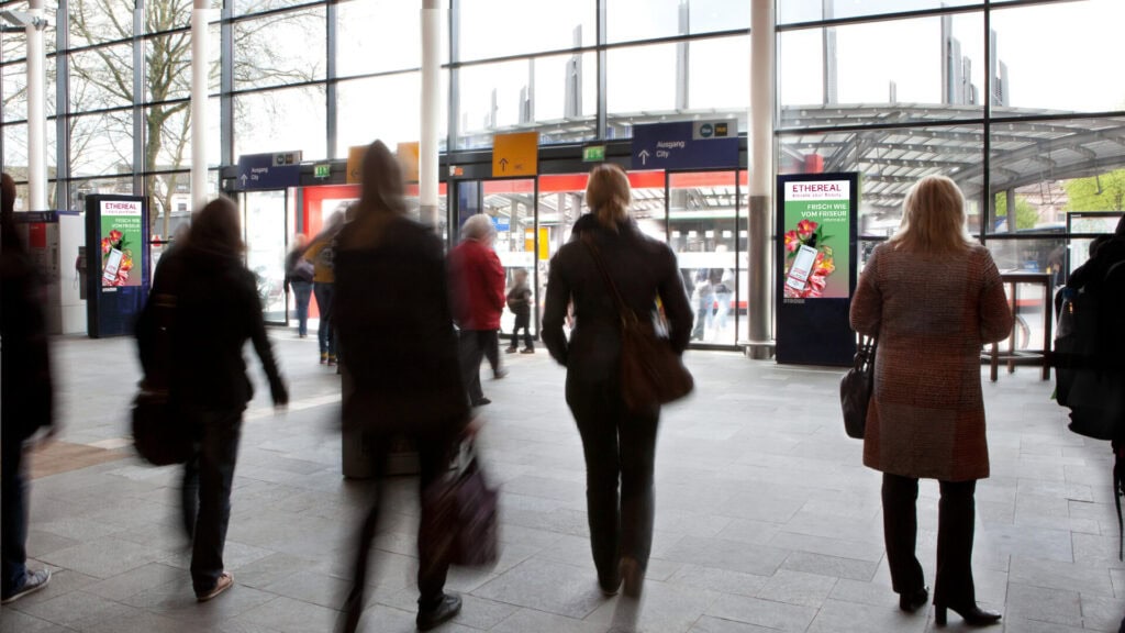 Eine Gruppe von Personen geht durch einen hell erleuchteten Bahnhofseingang, Silhouetten sichtbar.