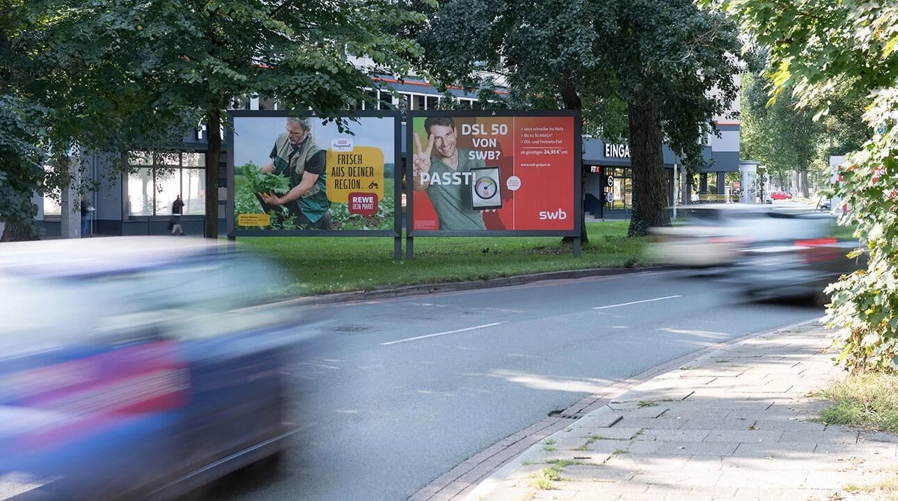 Eine befahrene Straße mit vorbeifahrenden Autos und Werbetafeln im Hintergrund.